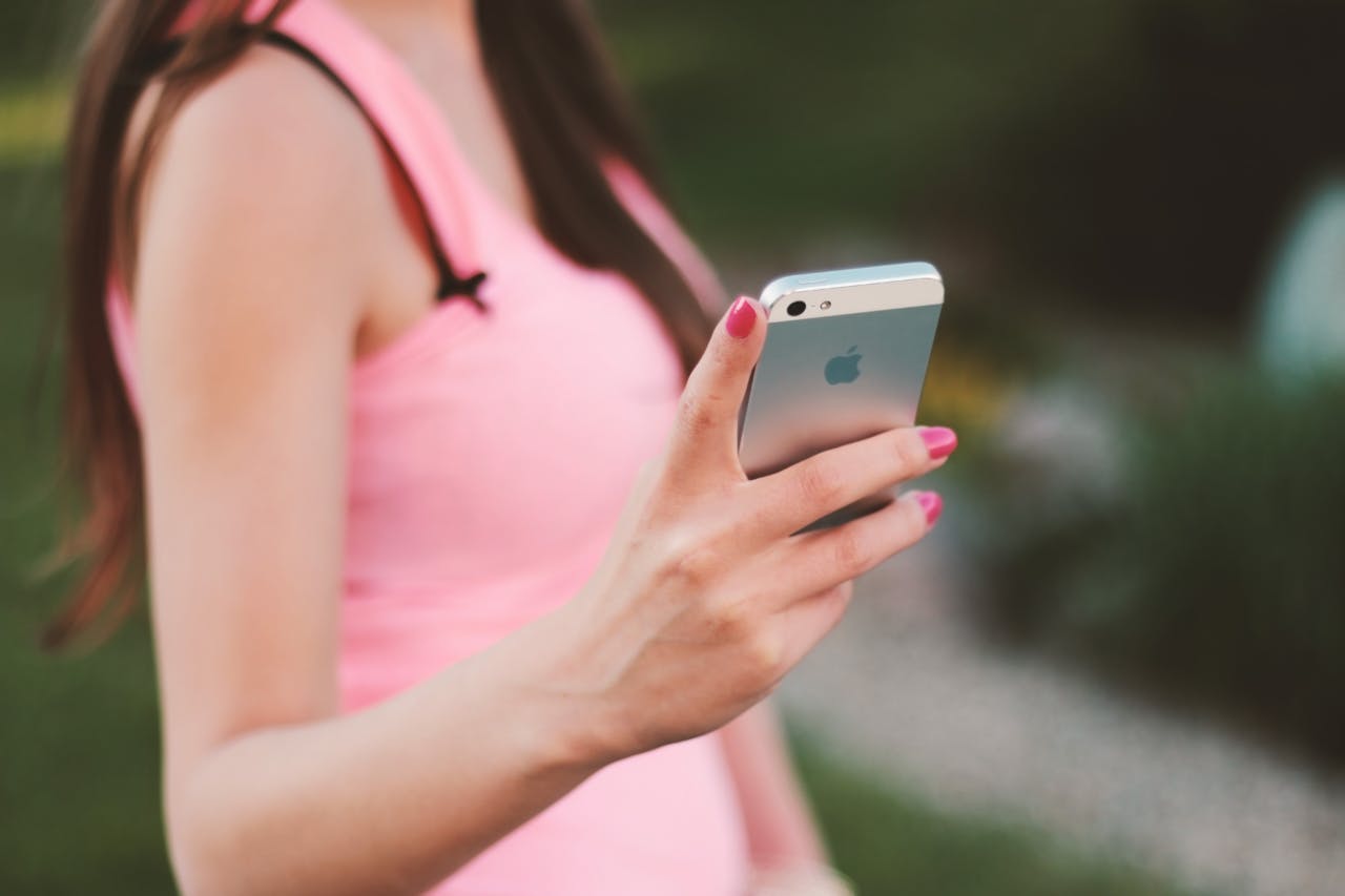 Close-up of a woman using a smartphone outdoors on a sunny day, wearing a pink tank top.